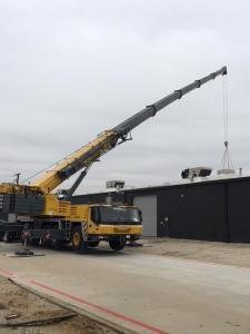 A crane loading HVAC equipment onto a building during a construction project in Dallas, TX.