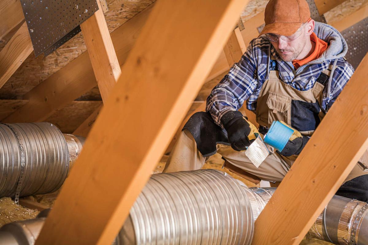 An HVAC technician applies duct tape to an attic hvac duct